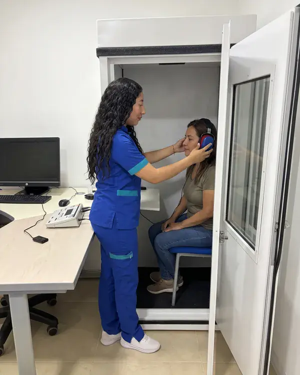 La fonoaudióloga le pone los audífonos a una paciente en la cabina de audiometría